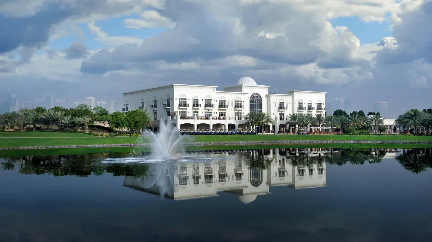 Address Montgomerie hotel in Dubai reflecting in the water with golf course and skyline.