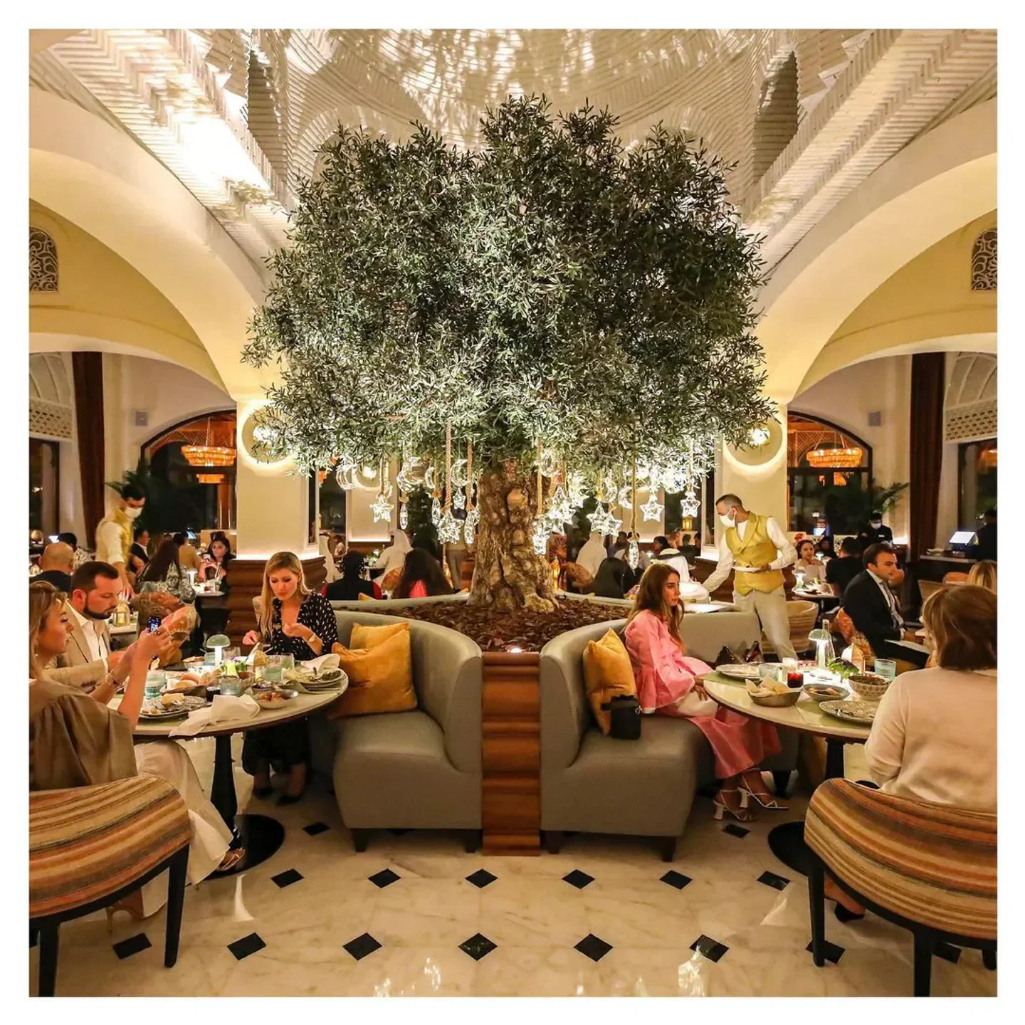 Dining scene at Al Nafoorah Dubai, showcasing a central tree feature and elegant ambiance.