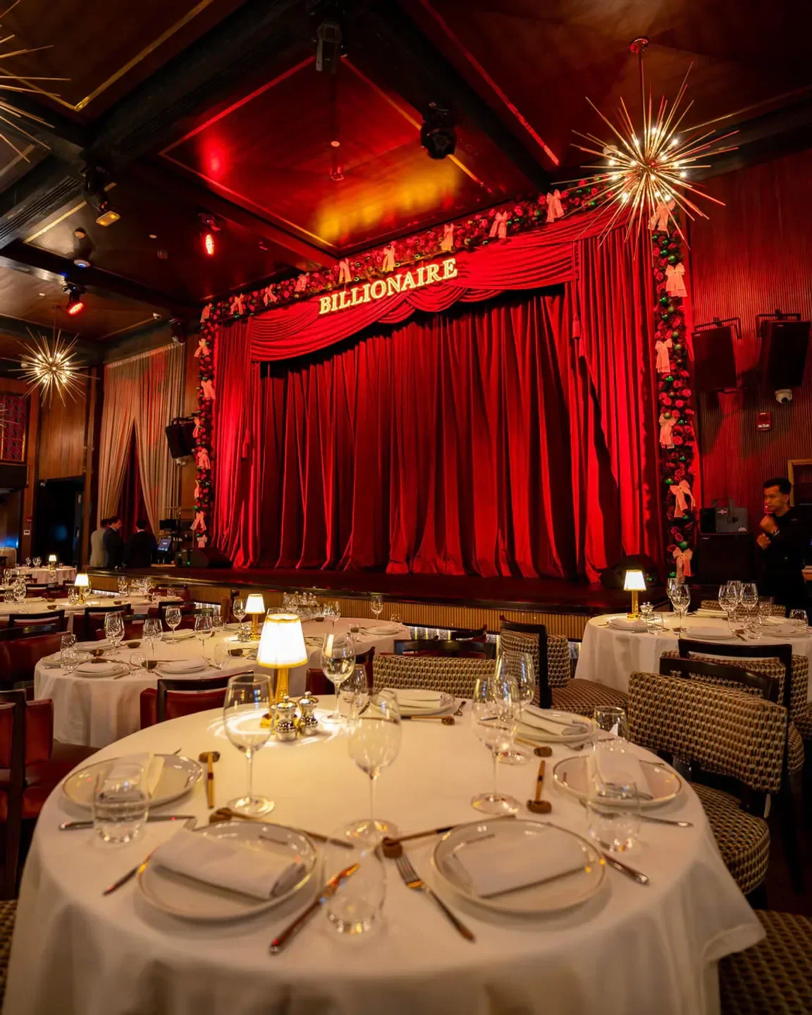 Elegant dining room at Billionaire restaurant in Dubai with stage and red curtains.