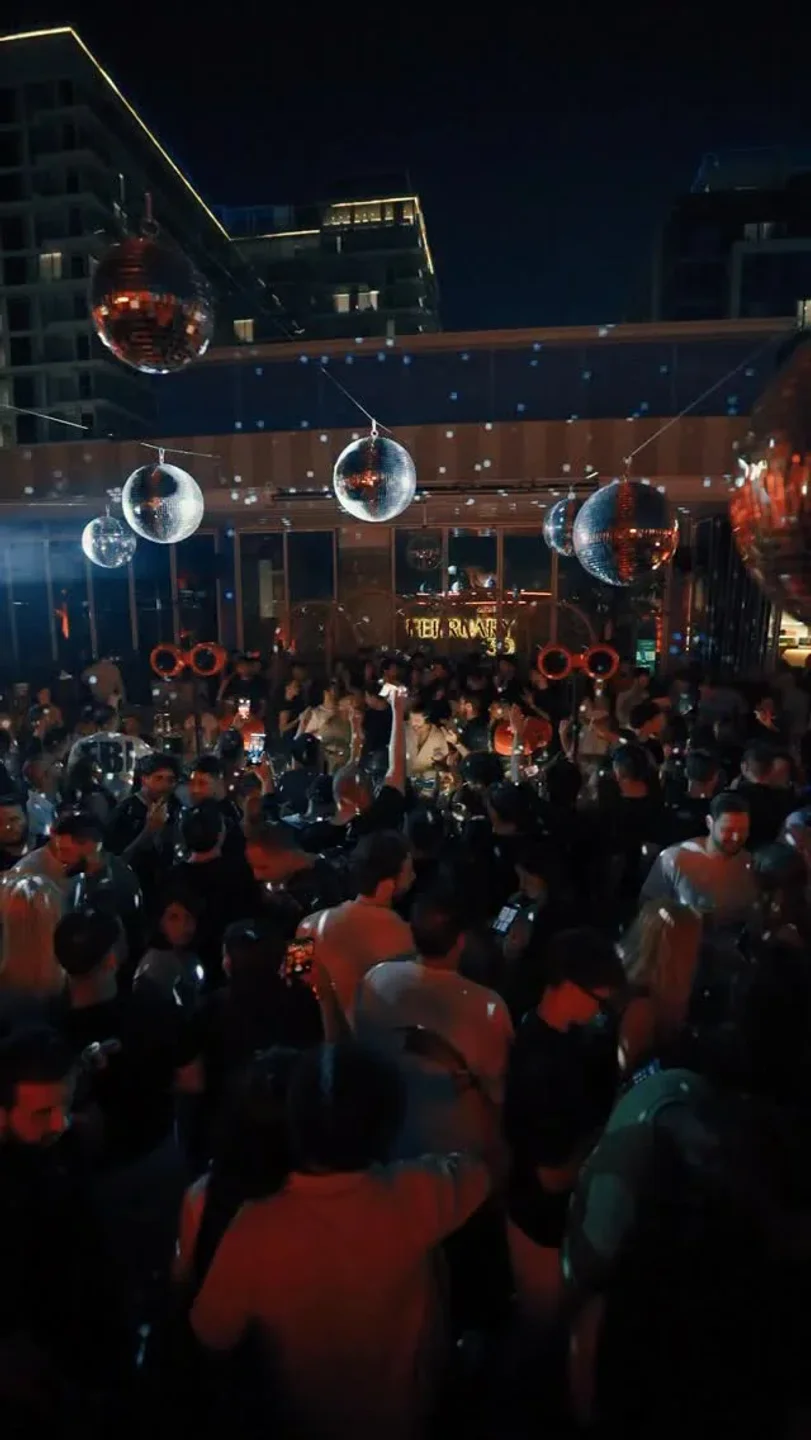 Crowd dancing under disco balls at February 30 beach club in the city at night.