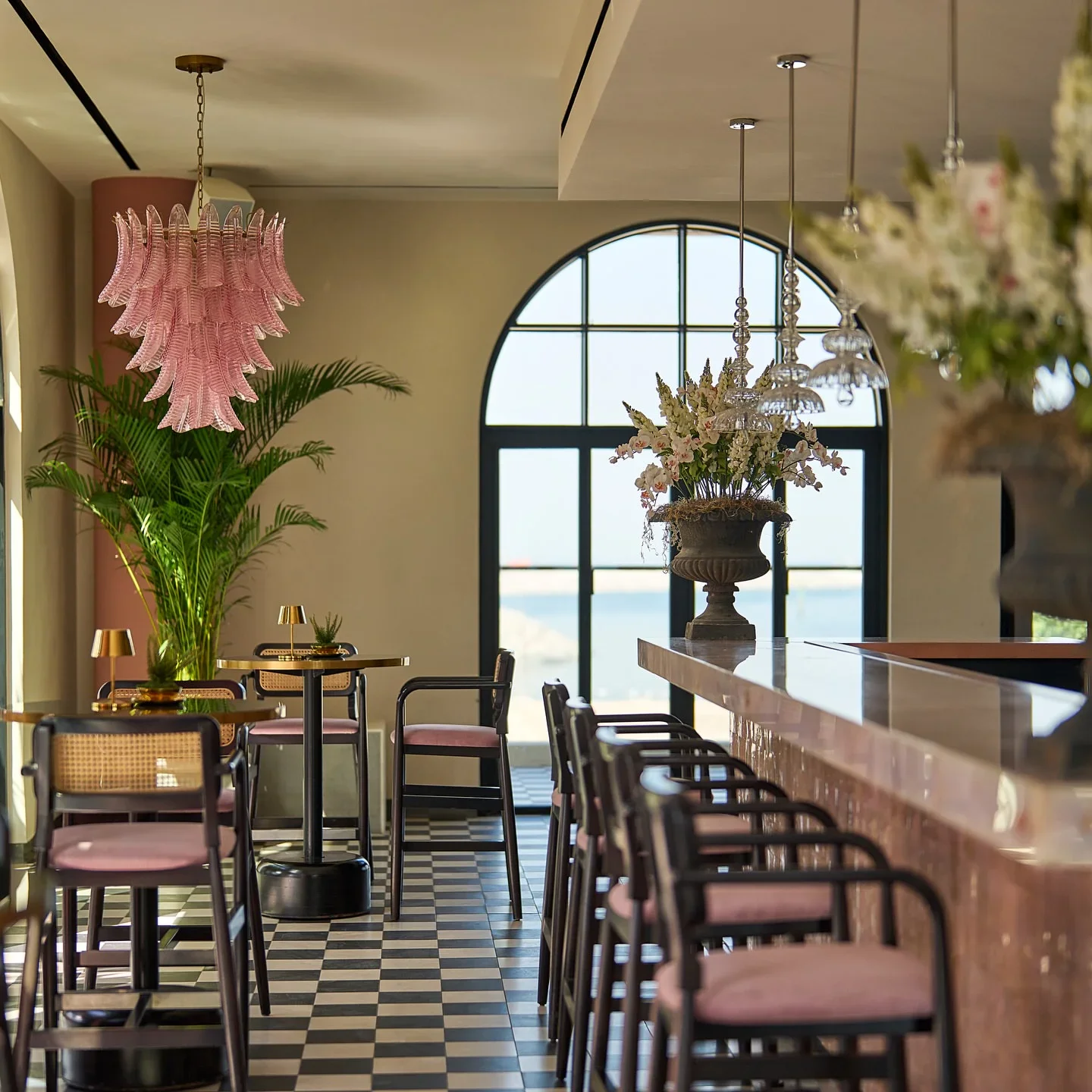 Gitano restaurant interior featuring pink chandelier, cane chairs, and a checkered floor with a view of the city.