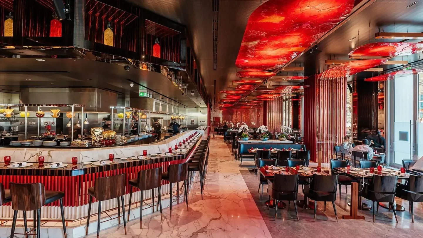 Elegant dining area at Joel Robuchon in Dubai, featuring a marble bar and red accents.