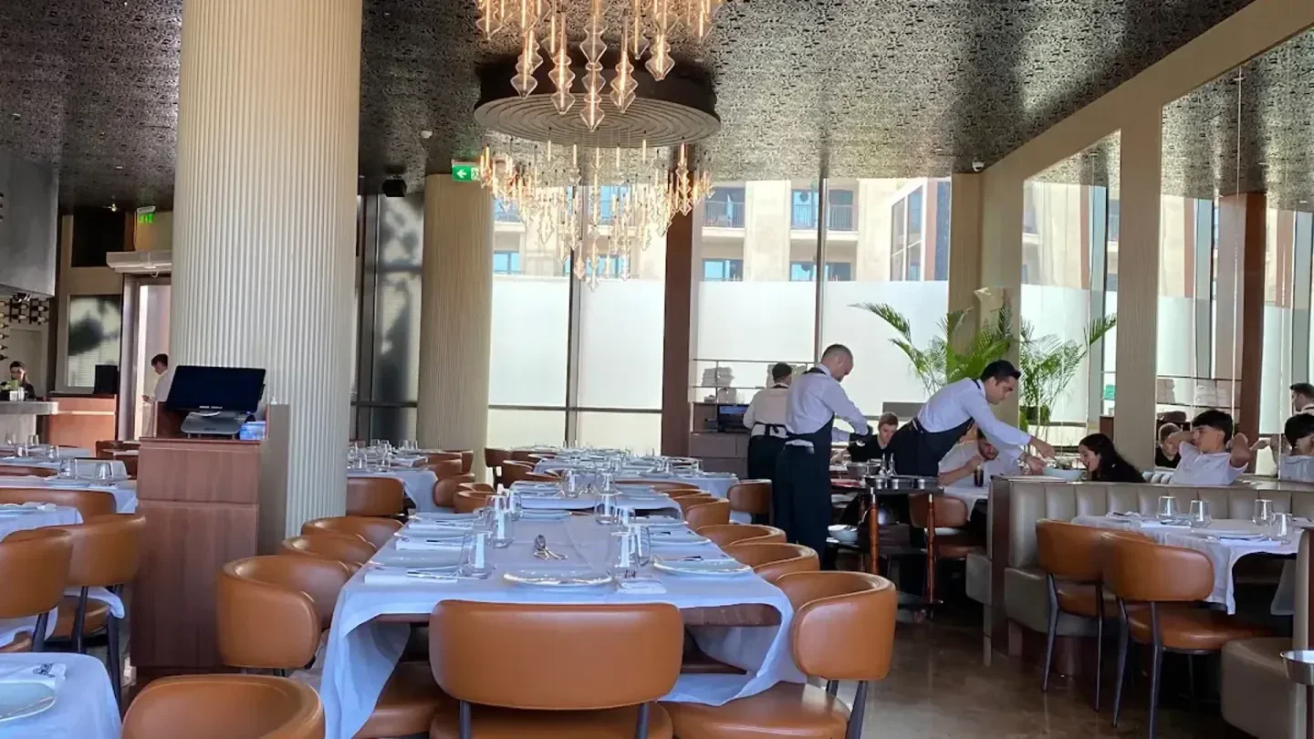 Inside Nusr-Et restaurant in Dubai with tables set, staff serving customers, and a chandelier.